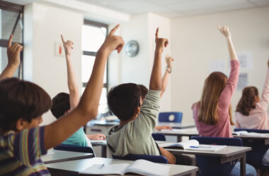 Jovens levantam a mão em sala de aula.