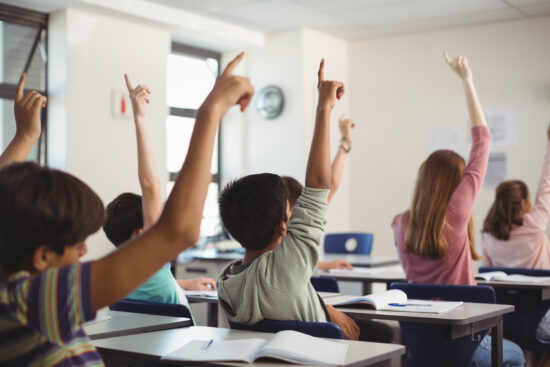 Jovens levantam a mão em sala de aula.